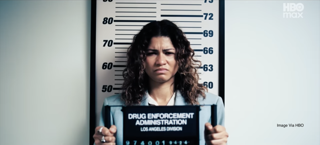 Rue Bennett holding a booking plate at her DEA arrest in Euphoria Season 3, Episode 4 "Kitty Likes to Dance